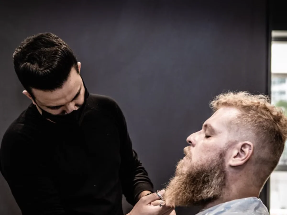 Barbeiro aparando e alinhando a barba de um cliente em ambiente profissional de barbearia (foto ilustrativa de banco de imagens).